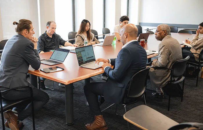 Students are seated around a table engaging with laptops